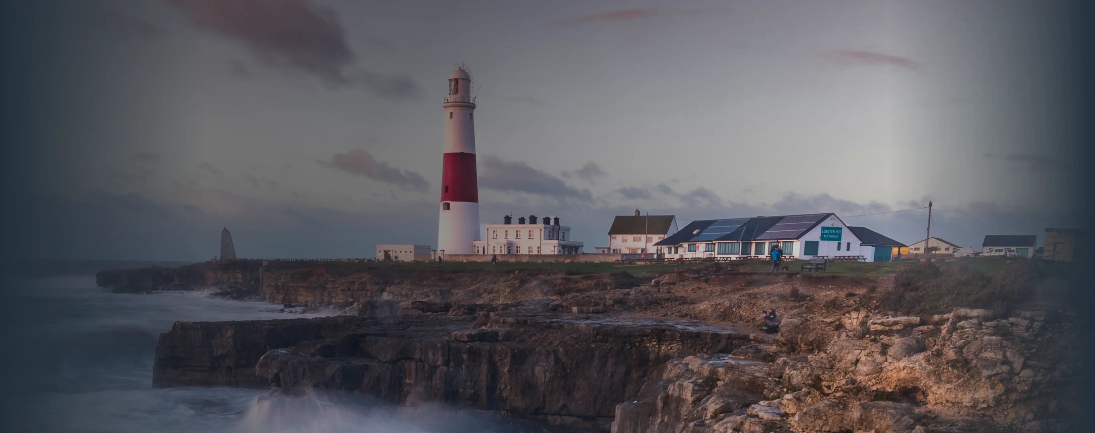 Las olas rompen en un acantilado británico con un faro en la distancia.