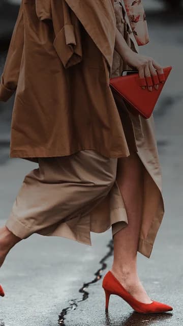 Una mujer bien vestida, con hermosos tacones altos rojos y un bolso rojo de moda, cruza la calle. Se superpone la frase francesa "bien habillé" con su traducción al español, "bien vestido".