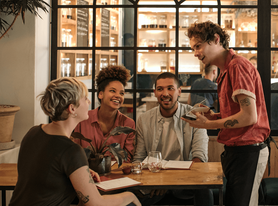 Un grupo de amigos practica un nuevo idioma que han aprendido mientras hacen un pedido a un camarero en un elegante café.