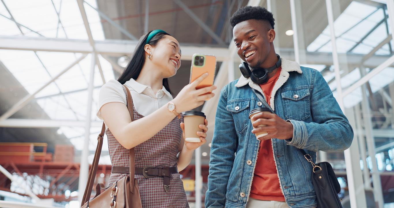 Dos estudiantes sonriendo y mirando un móvil representan los programas de aprendizaje de idiomas de Rosetta Stone para colegios, que promueven el aprendizaje interactivo y mediante el uso del móvil.
