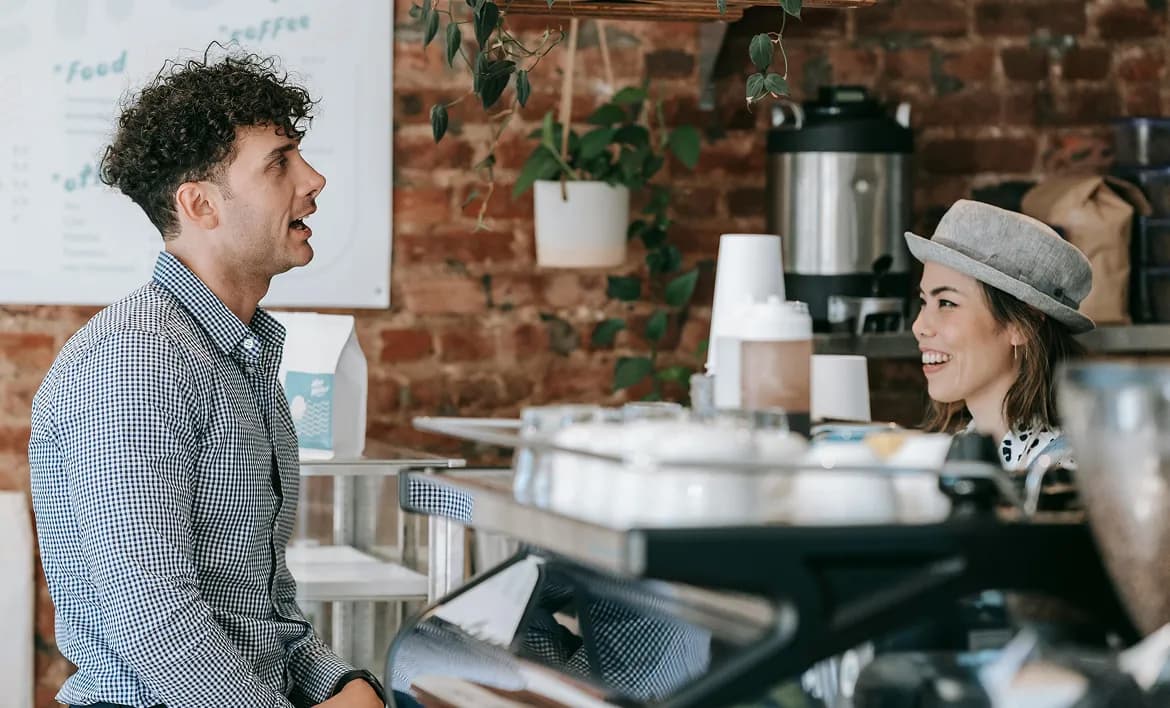 A man and woman smiling and conversing across a café counter.