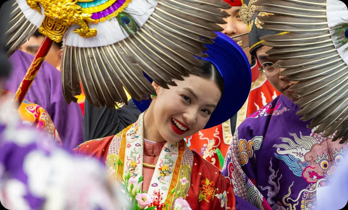 A smiling woman in vibrant traditional costume and headdress at a cultural celebration.